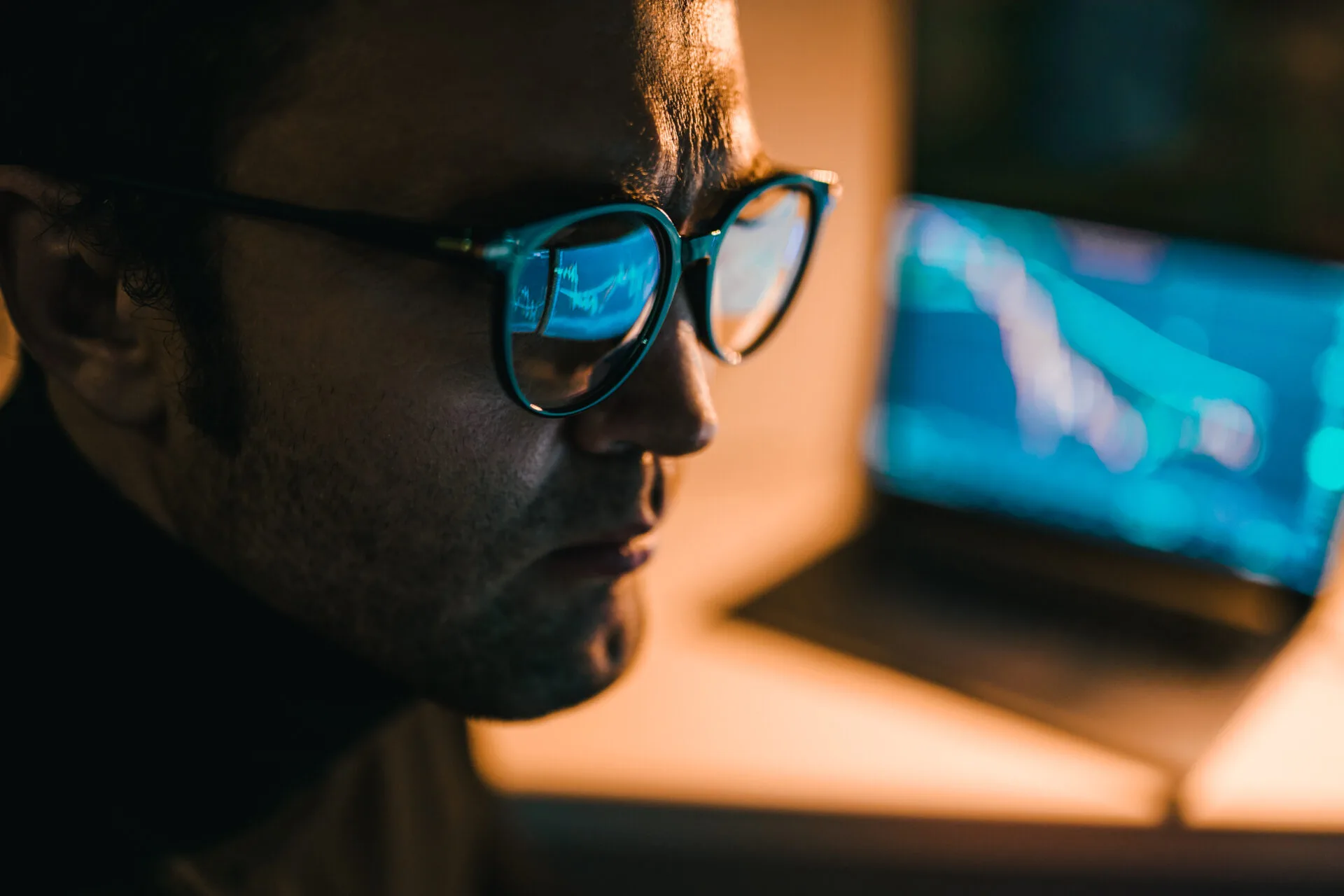 Pessoa usando óculos com filtro de luz azul enquanto trabalha em frente a múltiplos ecrãs em ambiente com pouca iluminação